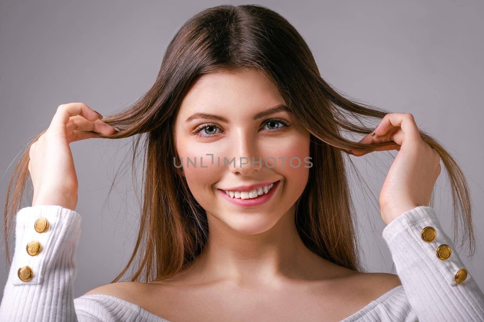 Delighted young girl with loose hair stands on a gray background looking happily at the camera
