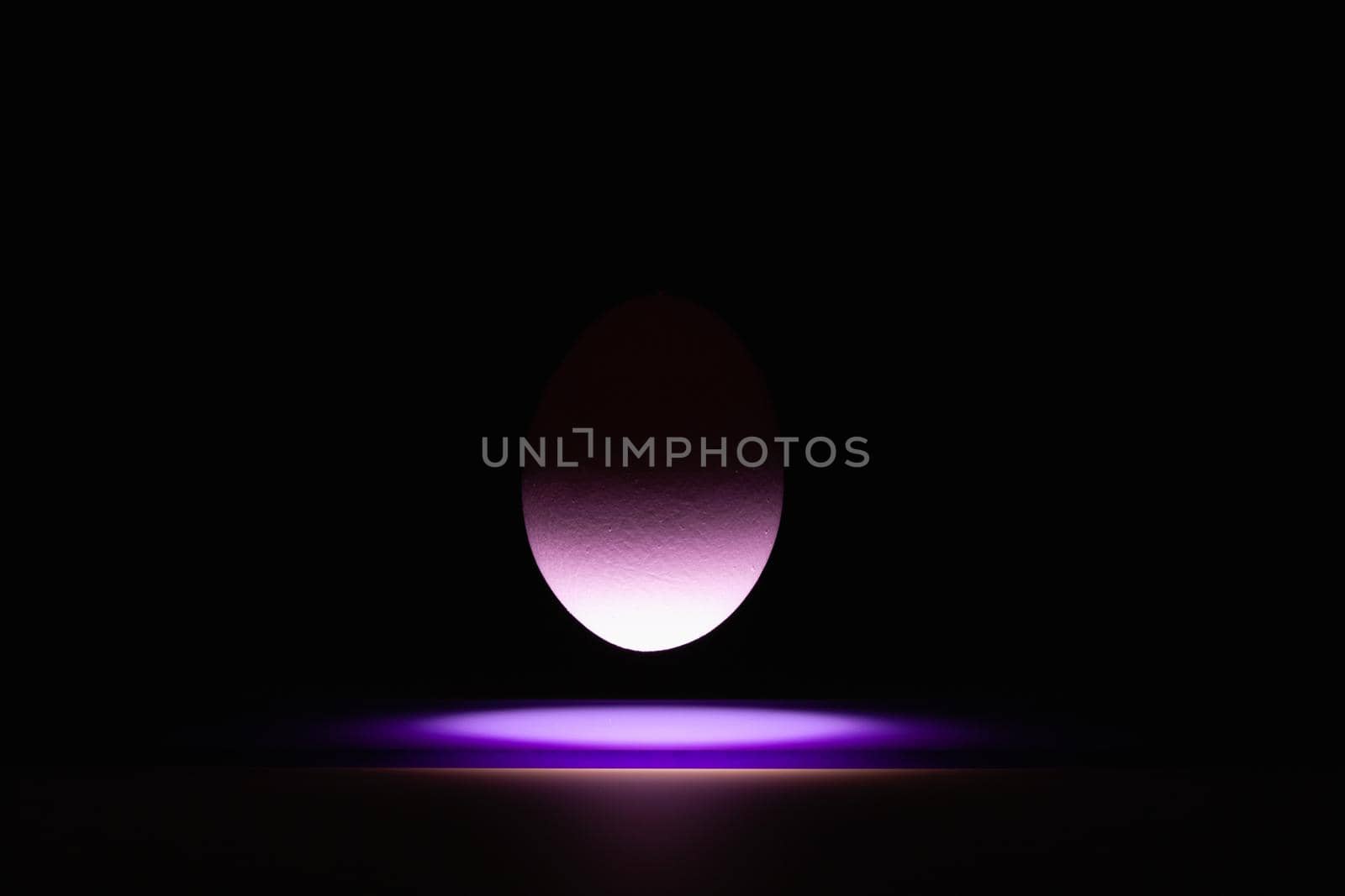 Purple egg levitating over a black glass table in the dark room.