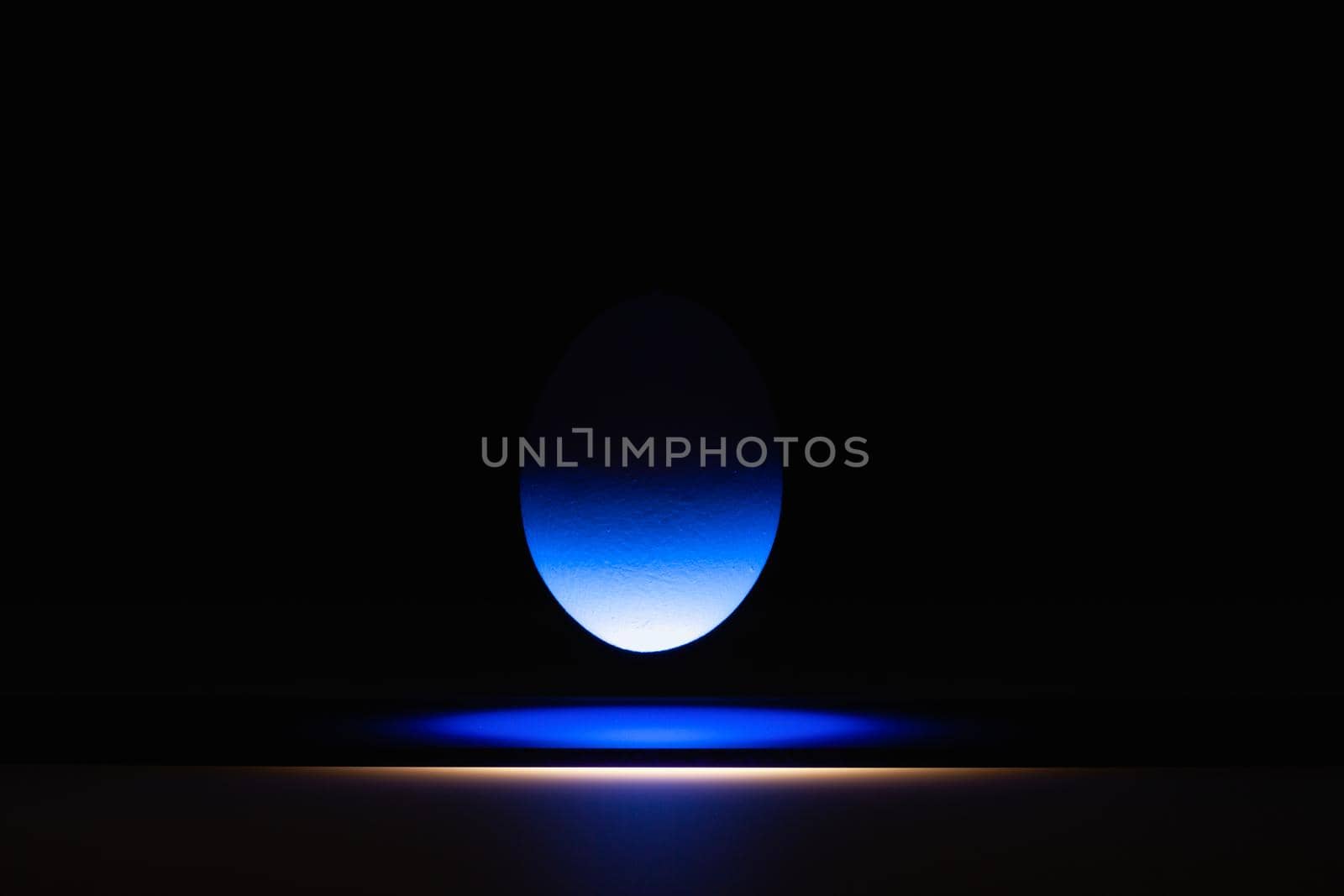 Blue egg levitating over a black glass table in the dark room.