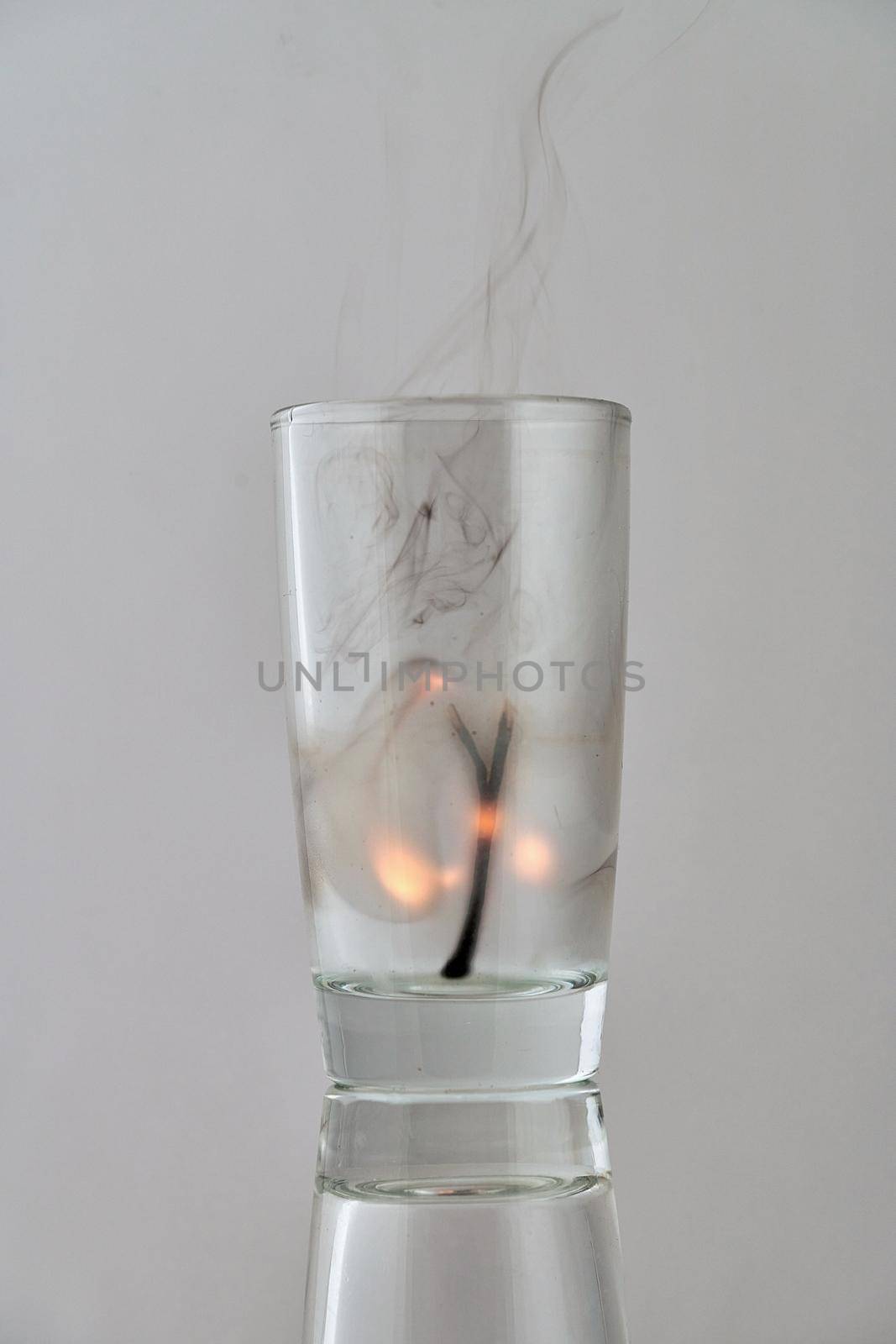 Remains of a dying match in a transparent glass on a light background. Concept, symbol