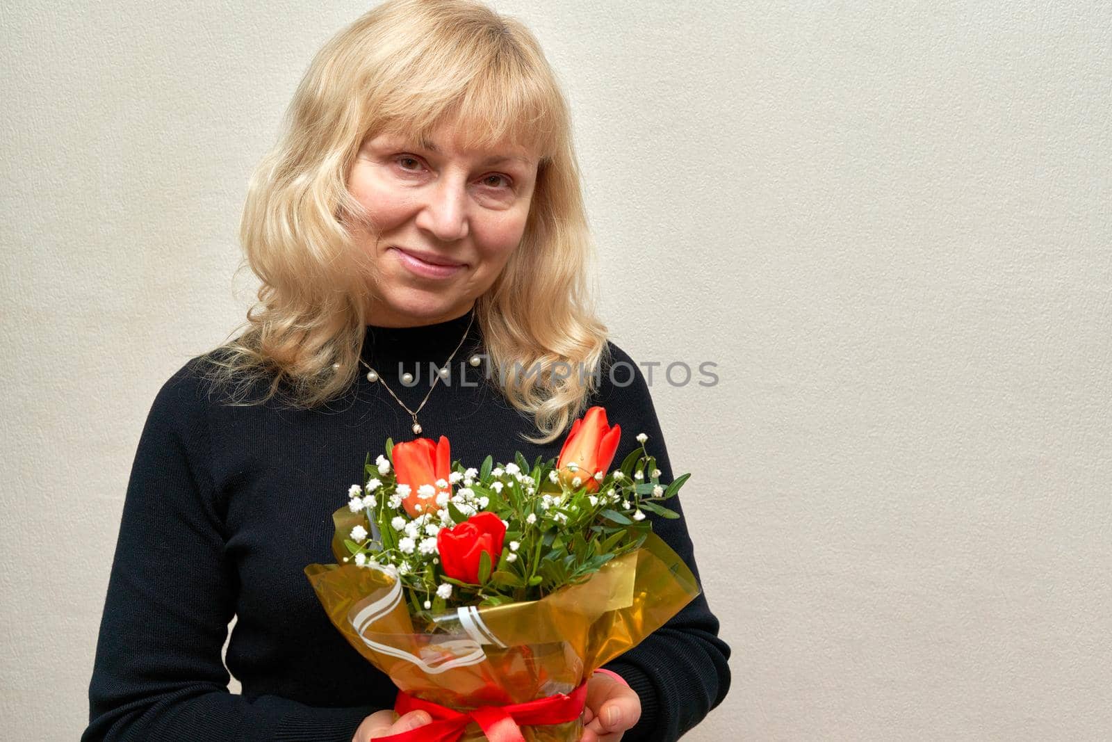 Portrait of a smiling woman of age with a bouquet of flowers. Blonde in black jumper with flowers