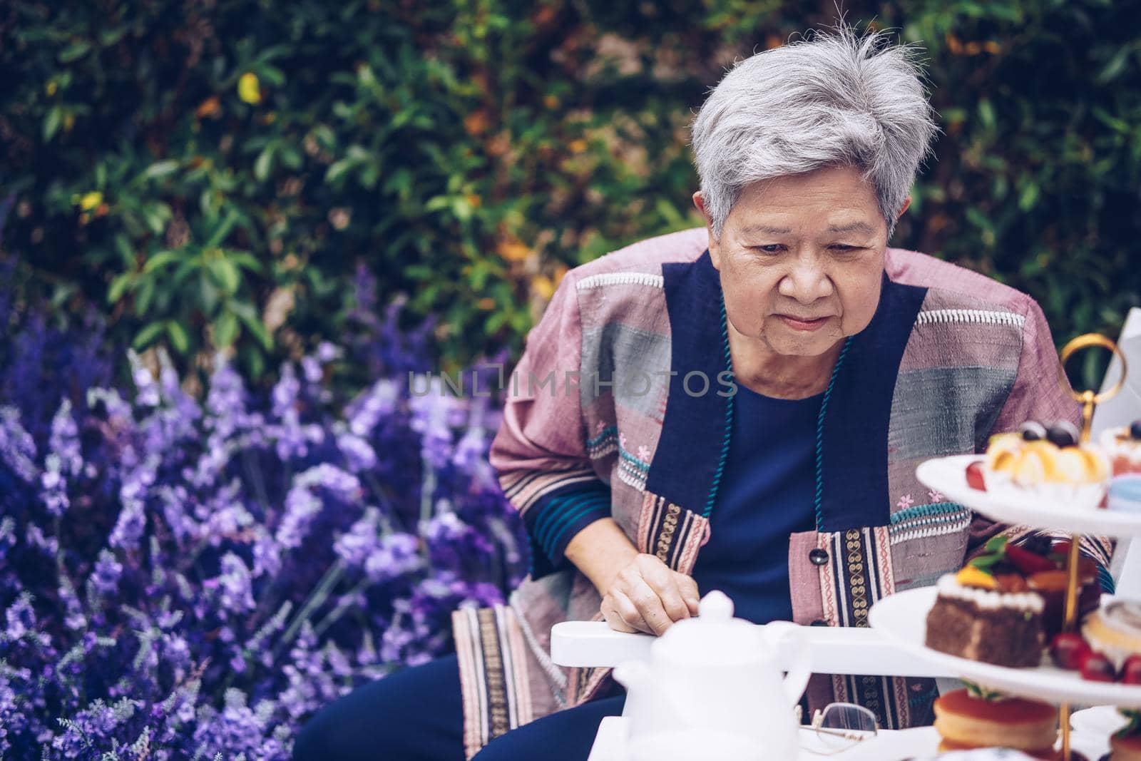 asian old elderly female elder woman resting relaxing in lavender flower garden. senior leisure lifestyle