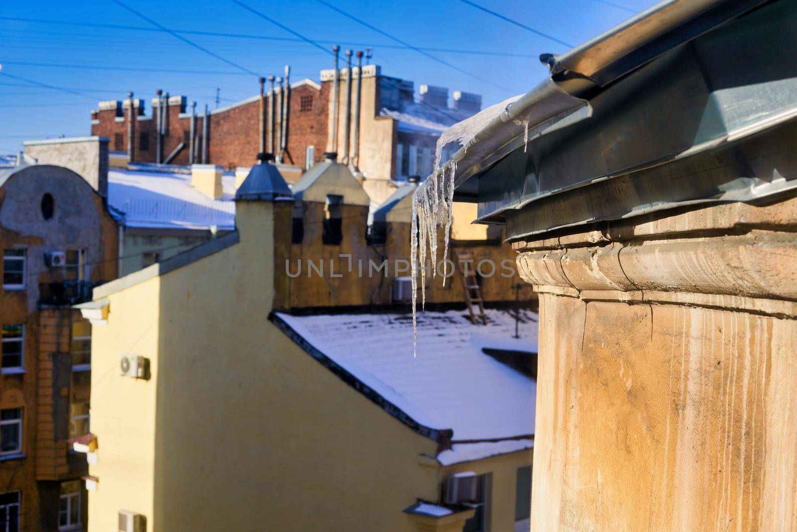 View of snow-covered roofs with spring icicles against blue sky by vizland