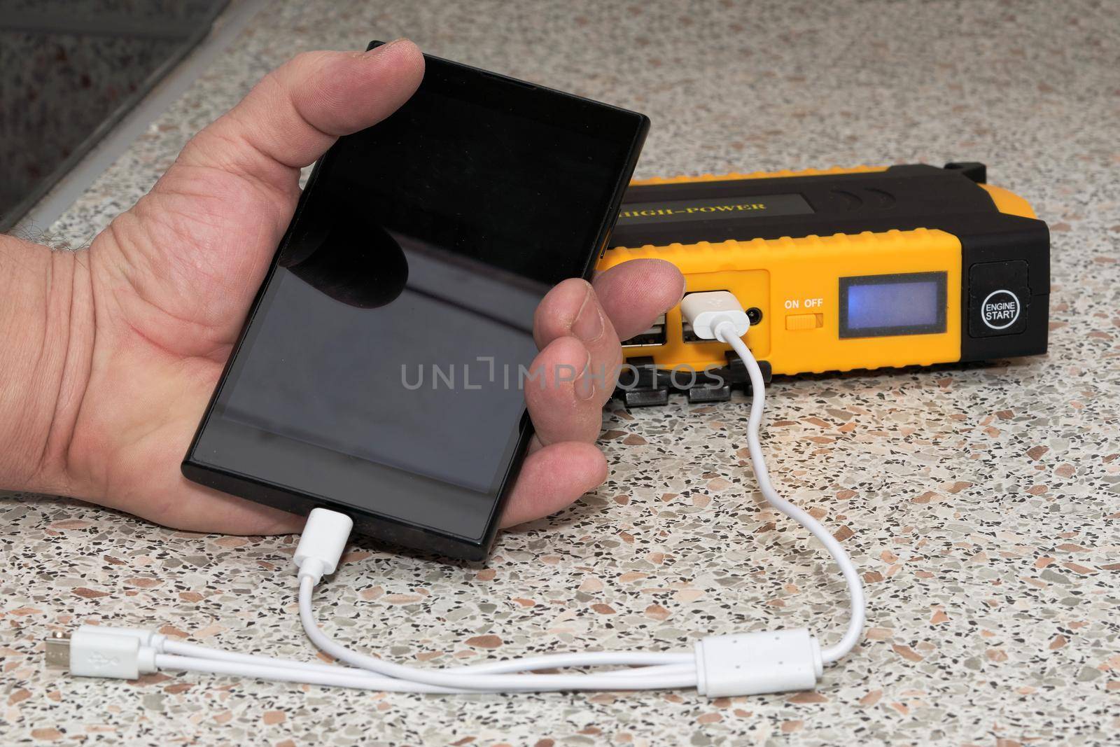 Hand holds black smartphone connected to large powerbank by white wire