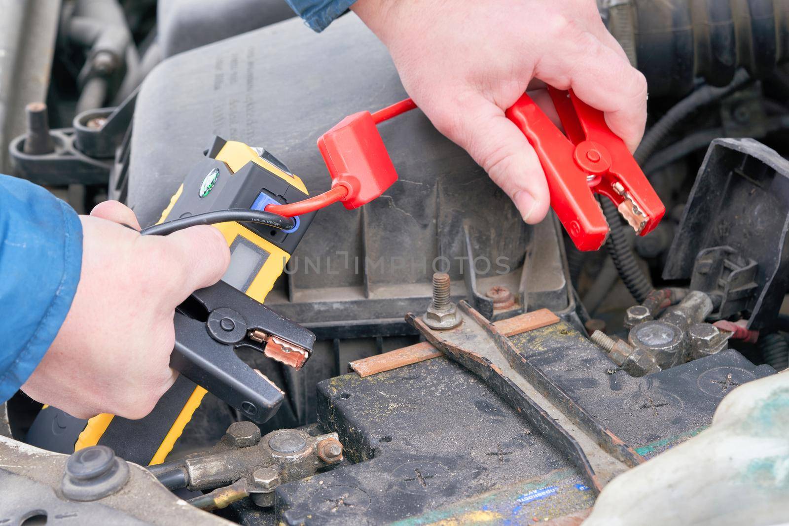 Hands connect the launcher clips to the car's battery