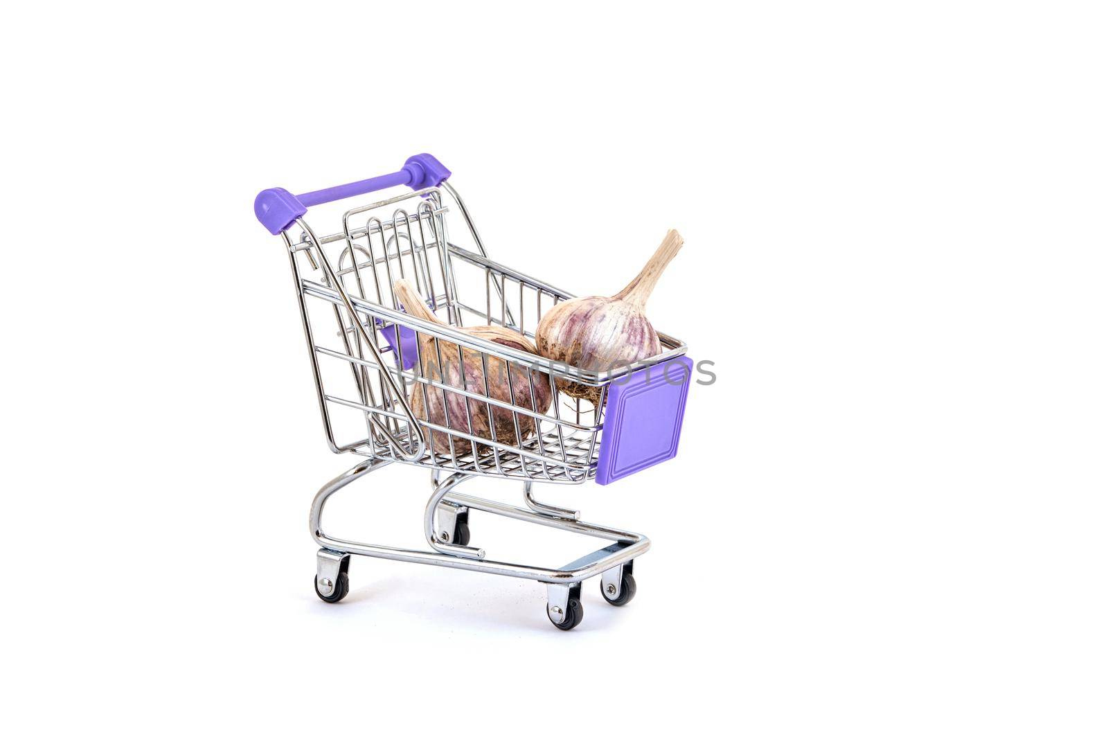 Ripe garlic lies in a small supermarket trolley on a white background, close up