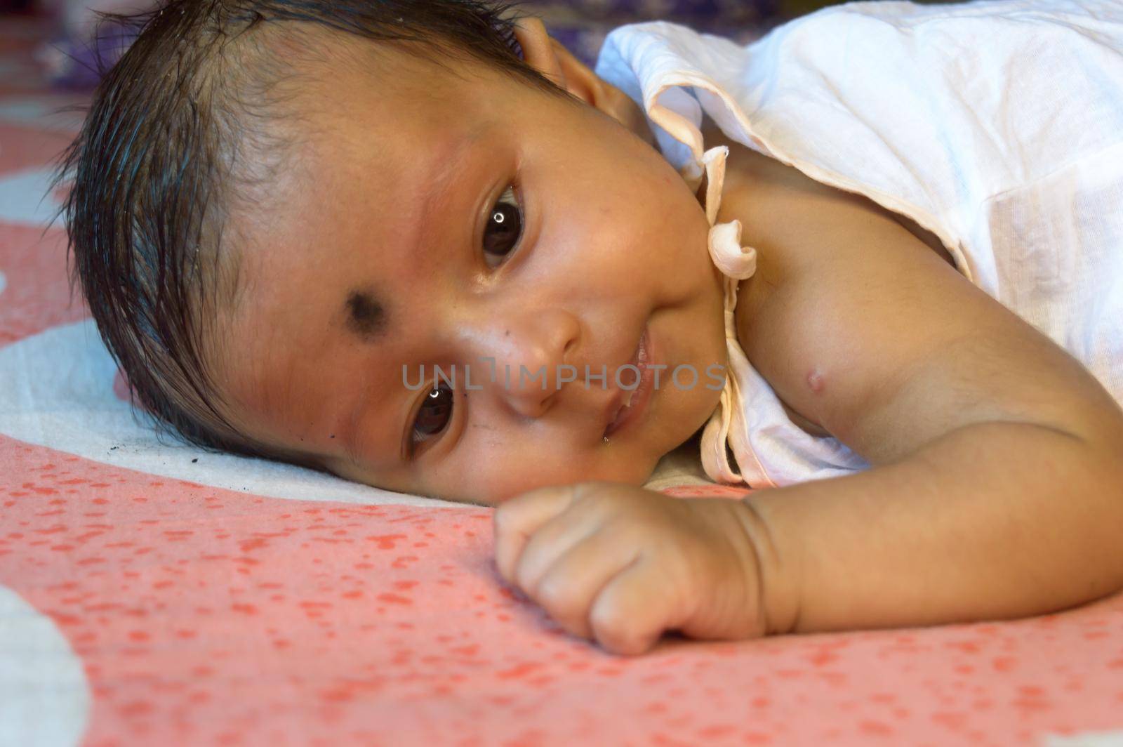 Close up face of cute newborn baby boy Lying On Front. One month old Sweet little infant toddler Closeup portrait. Indian ethnicity. Front view. Child care peace tranquil background.