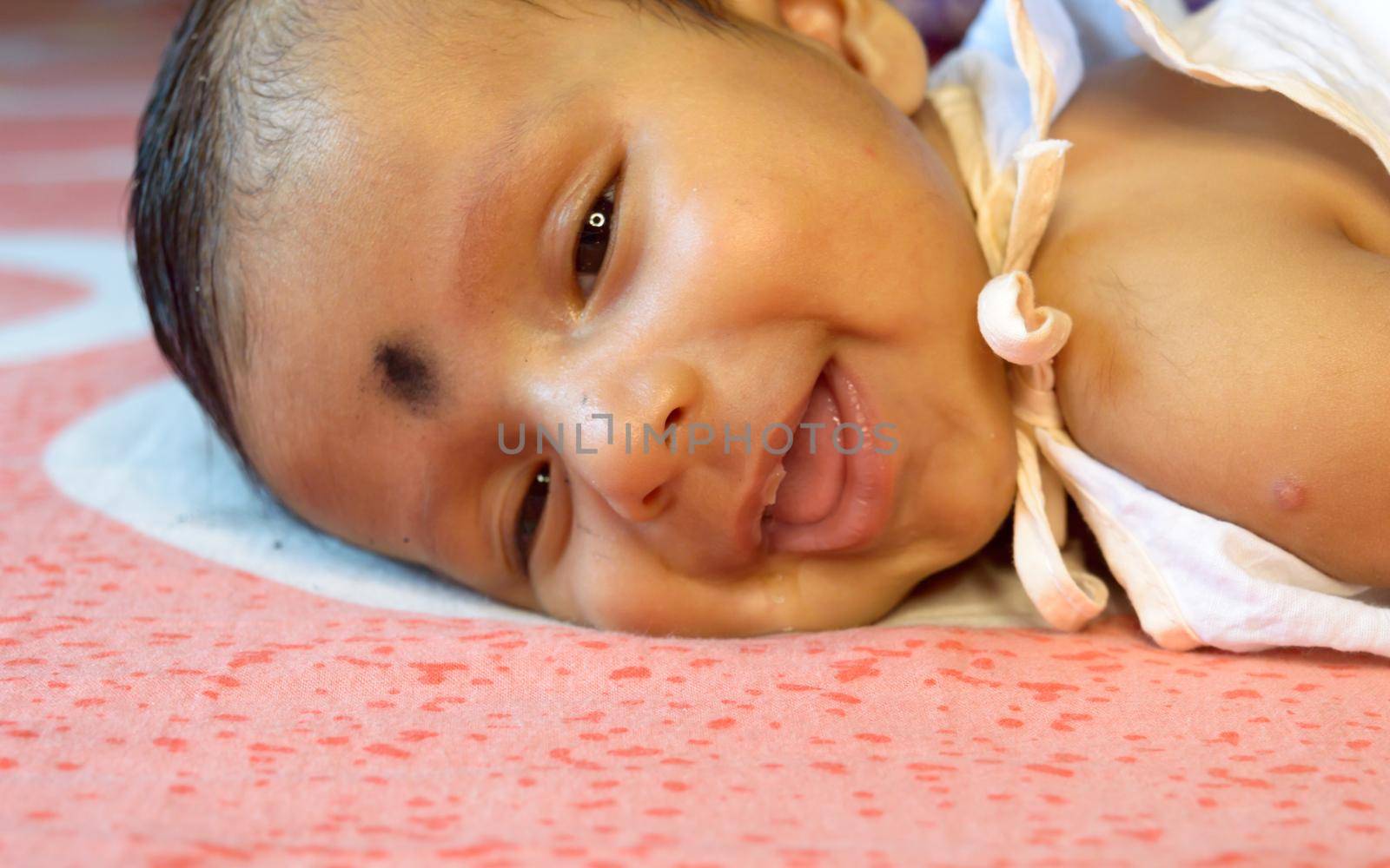 Close up face of cute newborn baby boy in smiling happy mood. One month old Sweet little infant toddler Closeup portrait. Indian ethnicity. Front view. Child care peace tranquil background. by sudiptabhowmick