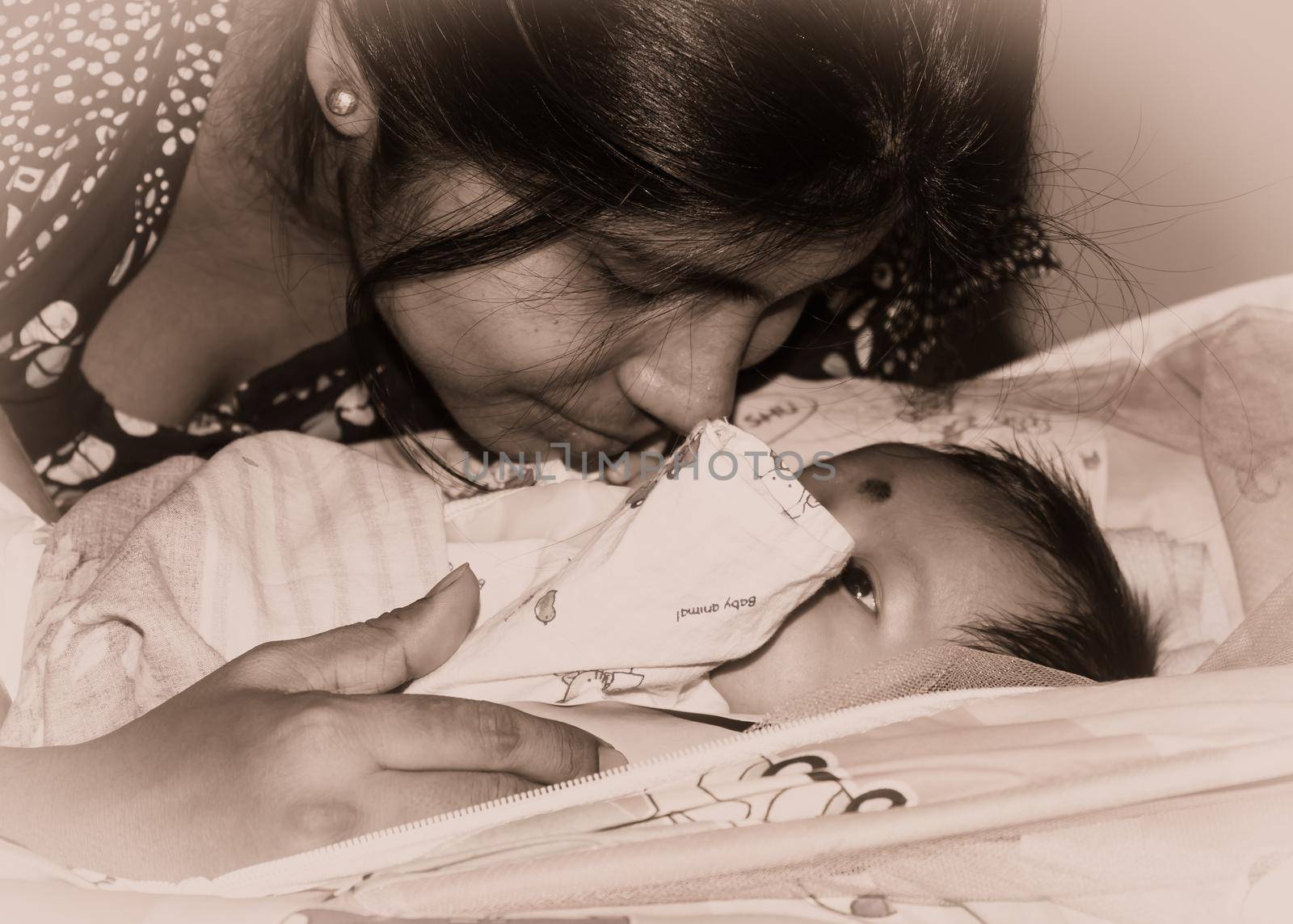 Cute newborn baby boy kissed by mother in her mother lap lying on bed. Close up. One month old Sweet little infant toddler. Indian ethnicity. Front view. Happy mother’s day background image.