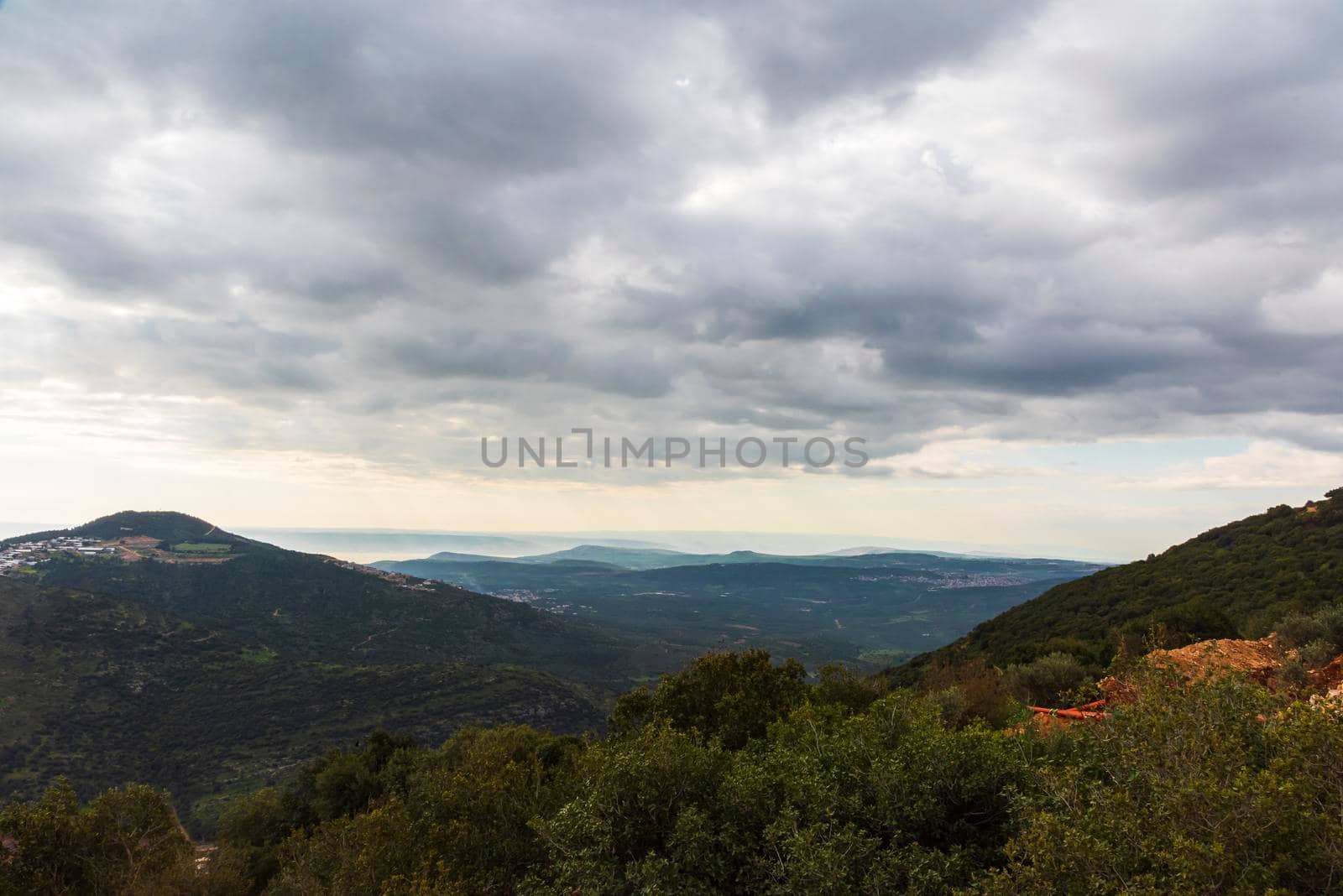 A view of a mountain range and a green valley in the morning at sunrise, against a dramatic backdrop of blue skies and clouds. North District Israel. High quality photo. Travel concept hiking