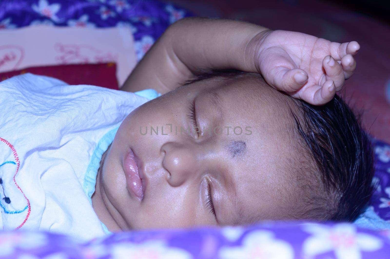 Close up face of a cute sleeping newborn baby. Closeup portrait of a Sweet just born infant boy captured in sleepy mood drowsy eyes. Hand on Head. Front view. Child care kid background image. by sudiptabhowmick