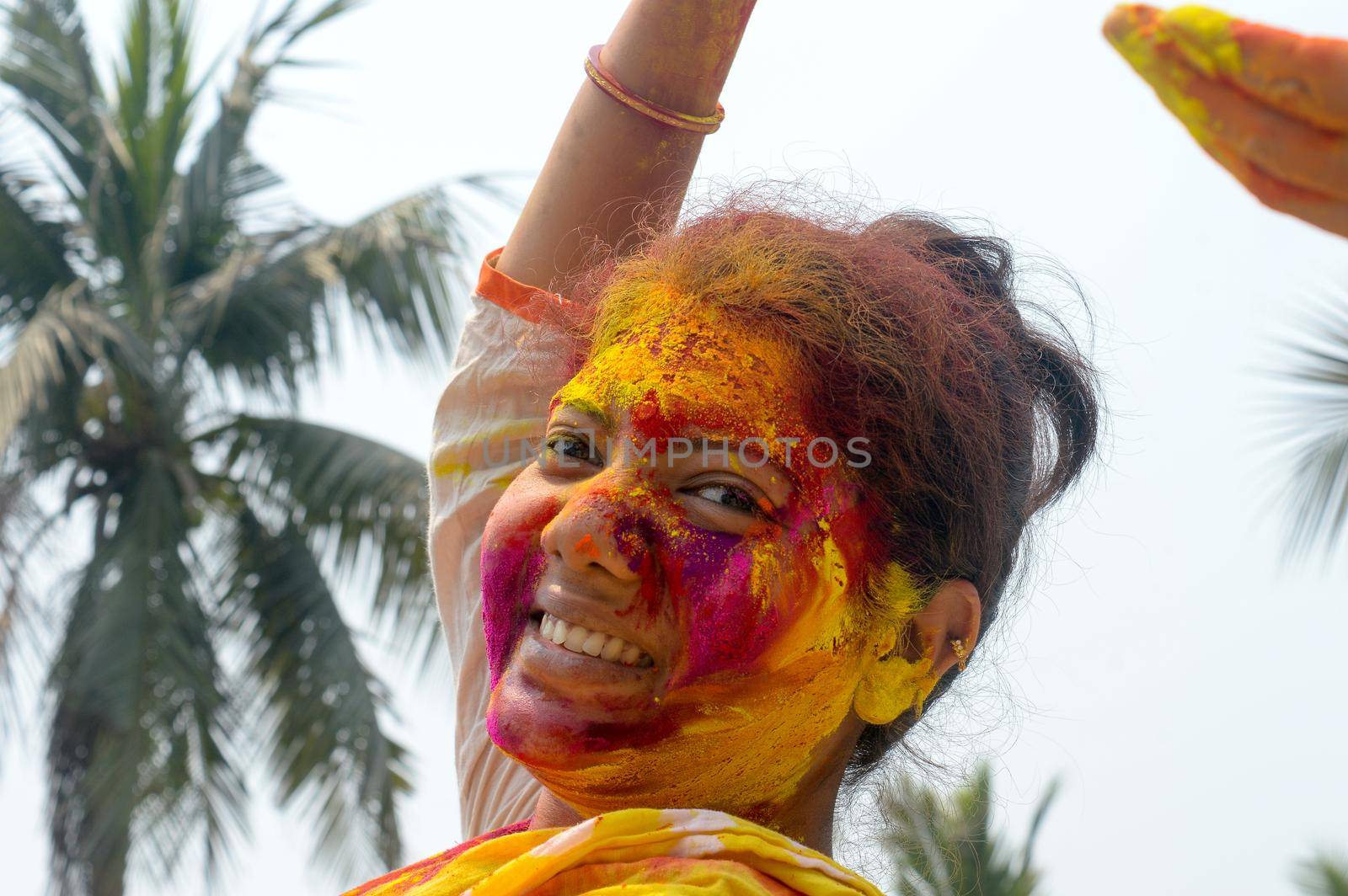 Portrait Of One Young Indian Happy woman with pink, yellow and red Holi colored powder paint on face During Holi Color festival. Front View. Looking at camera.