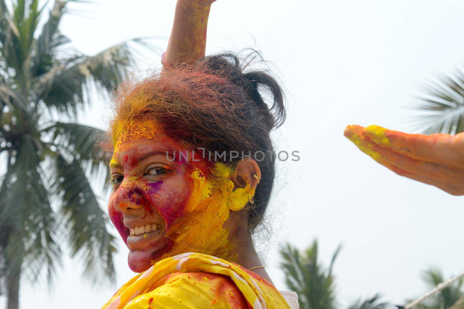 Portrait Of One Young Indian Happy woman with pink, yellow and red Holi colored powder paint on face During Holi Color festival. Front View. Looking at camera.