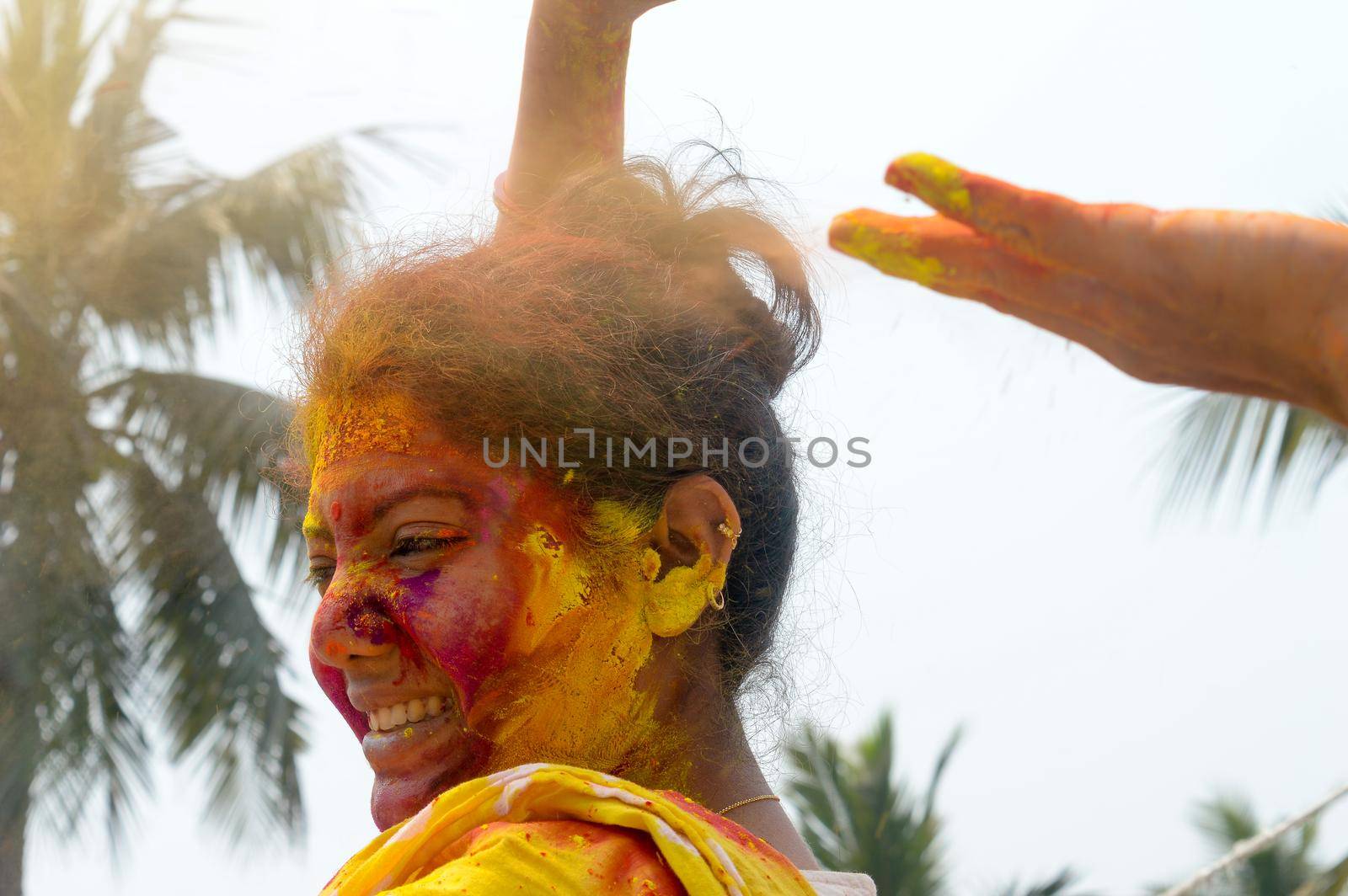 Portrait Of One Young Indian Happy woman with pink, yellow and red Holi colored powder paint on face During Holi Color festival. Front View. Looking at camera. by sudiptabhowmick
