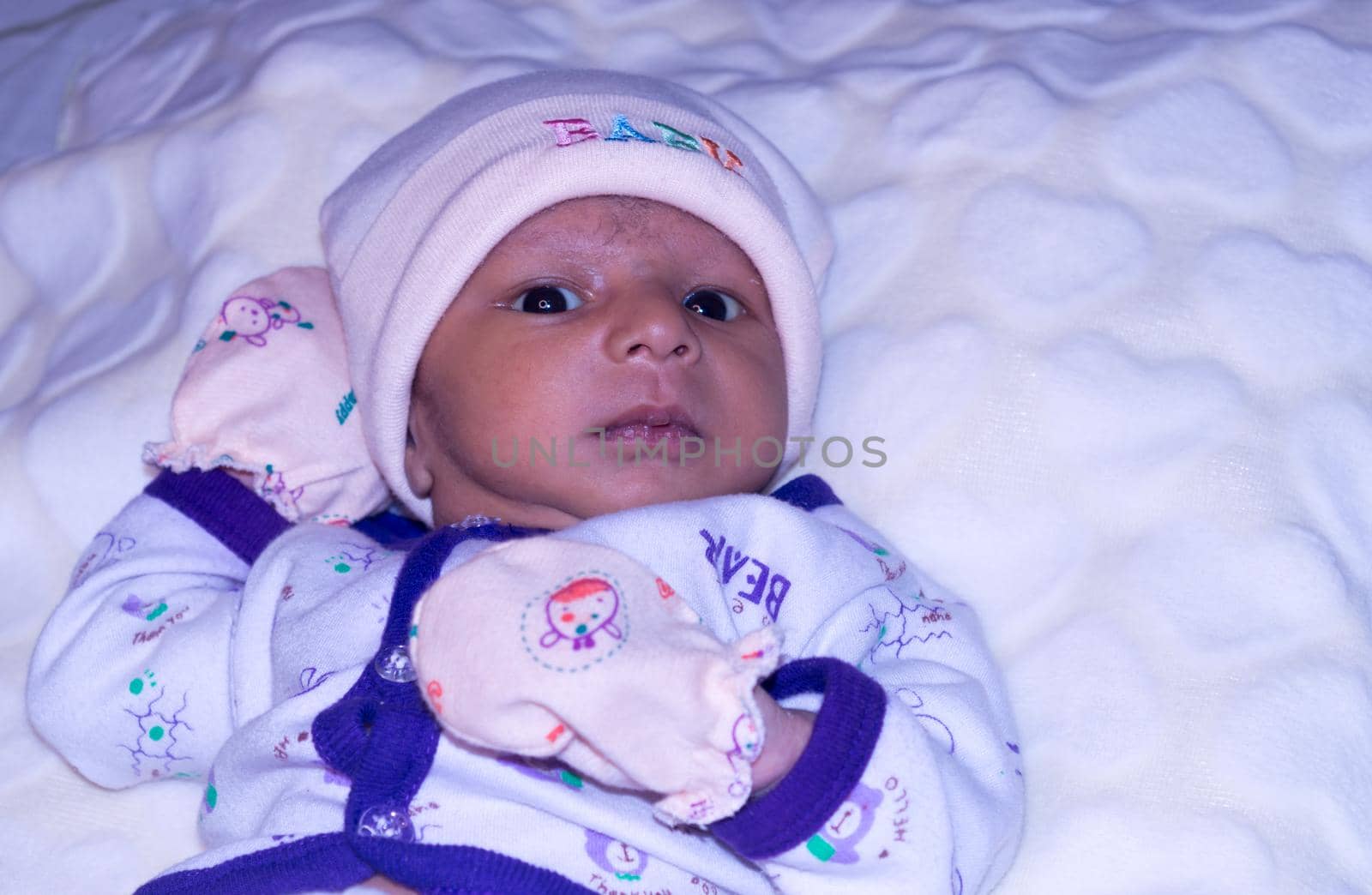 Closeup portrait image of cute beautiful adorable baby boy Asian and Indian ethnicity in winter clothing lying of bed on white blanket. One month old Sweet toddler posing looking at camera. Front View by sudiptabhowmick
