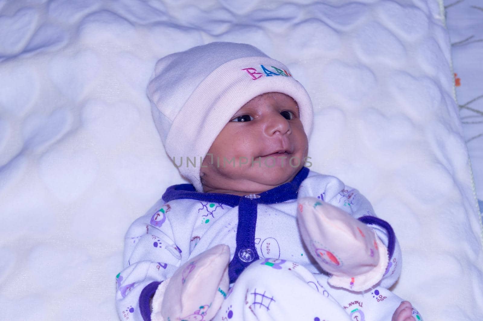 Closeup portrait image of cute beautiful adorable baby boy Asian and Indian ethnicity in winter clothing lying of bed on white blanket. One month old Sweet toddler posing on playing mood. Front View.
