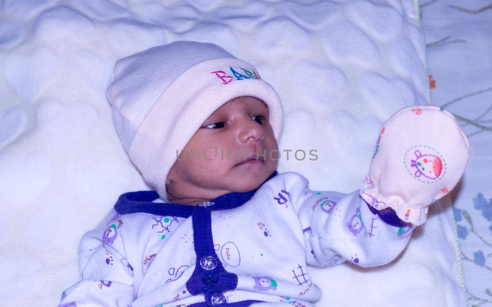 Closeup portrait image of cute beautiful adorable baby boy Asian and Indian ethnicity in winter clothing lying of bed on white blanket. One month old Sweet toddler posing on playing mood. Front View.