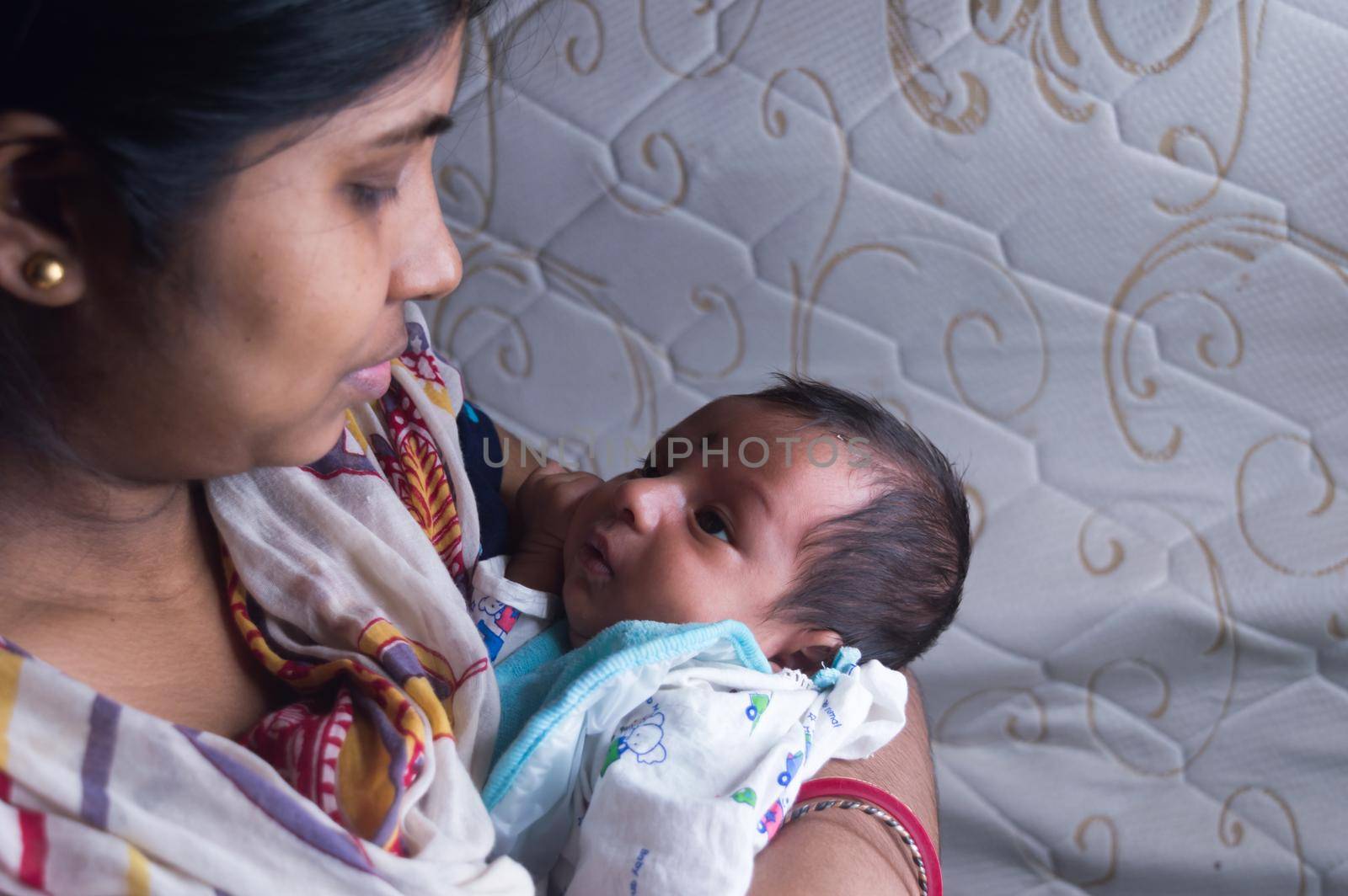 Close up face of a cute newborn baby boy happily looks at his mother in her mother lap. One month old Sweet little infant toddler. Indian ethnicity. Front view. Happy mother’s day background image.