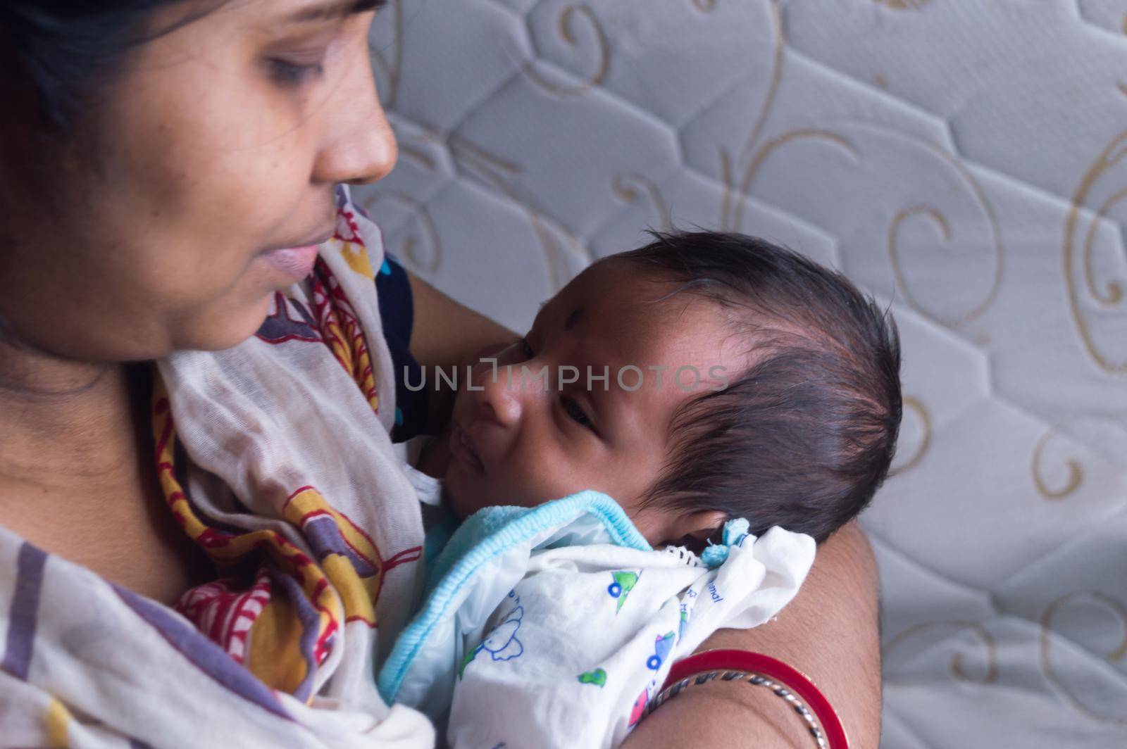 Close up face of a cute newborn baby boy happily looks at his mother in her mother lap. One month old Sweet little infant toddler. Indian ethnicity. Front view. Happy mother’s day background image.