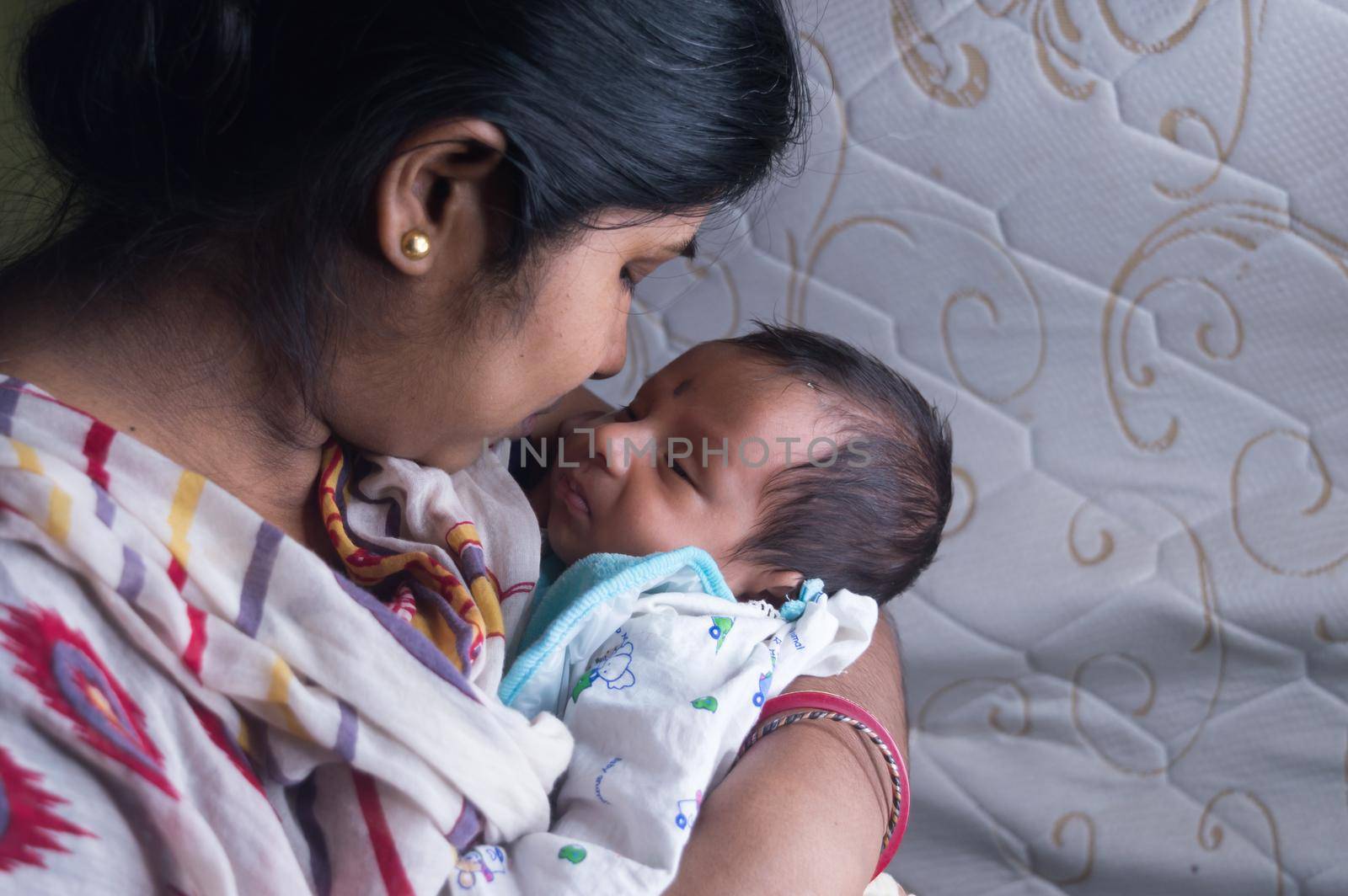 Close up face of a cute newborn baby boy kissed by her mother holding in her mother lap. One month old Sweet little infant toddler. Indian ethnicity. Front view. Happy mother’s day background image.