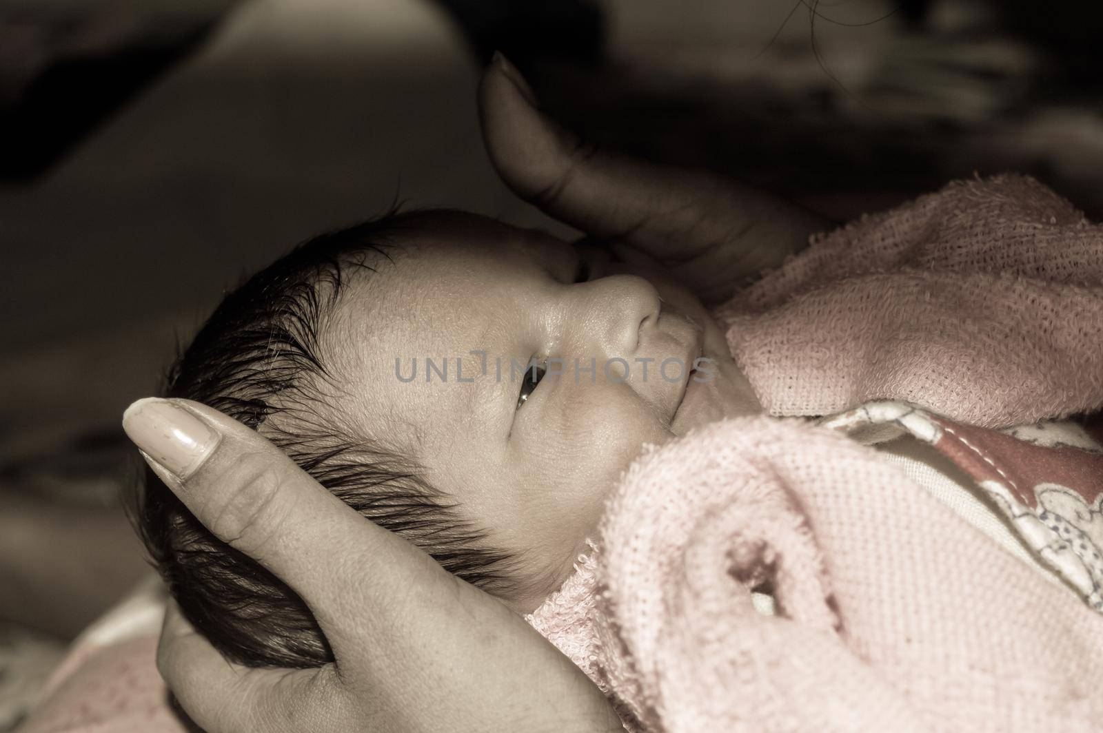 Beautiful Newborn baby boy closeup (6 days old) lying in mother lap in prenatal hospital. Kid wrapped in baby blanket (warm clothing) smiling and looking. His mother consoling and resting her baby.