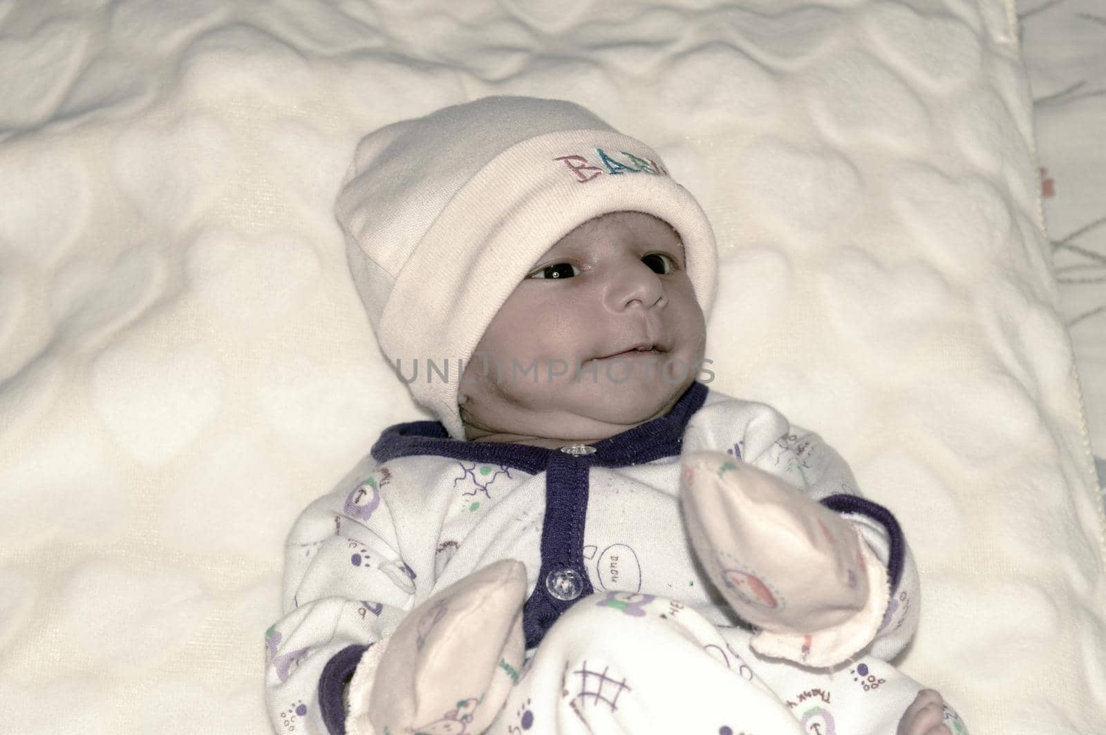 Closeup portrait image of cute beautiful adorable baby boy Asian and Indian ethnicity in winter clothing lying of bed on white blanket. One month old Sweet toddler posing on playing mood. Front View.