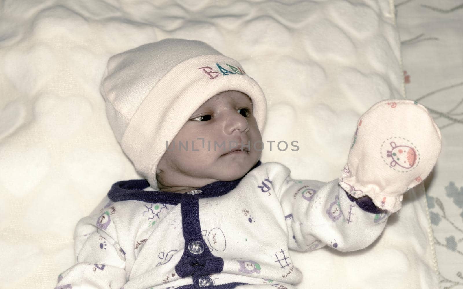Closeup portrait image of cute beautiful adorable baby boy Asian and Indian ethnicity in winter clothing lying of bed on white blanket. One month old Sweet toddler posing on playing mood. Front View. by sudiptabhowmick