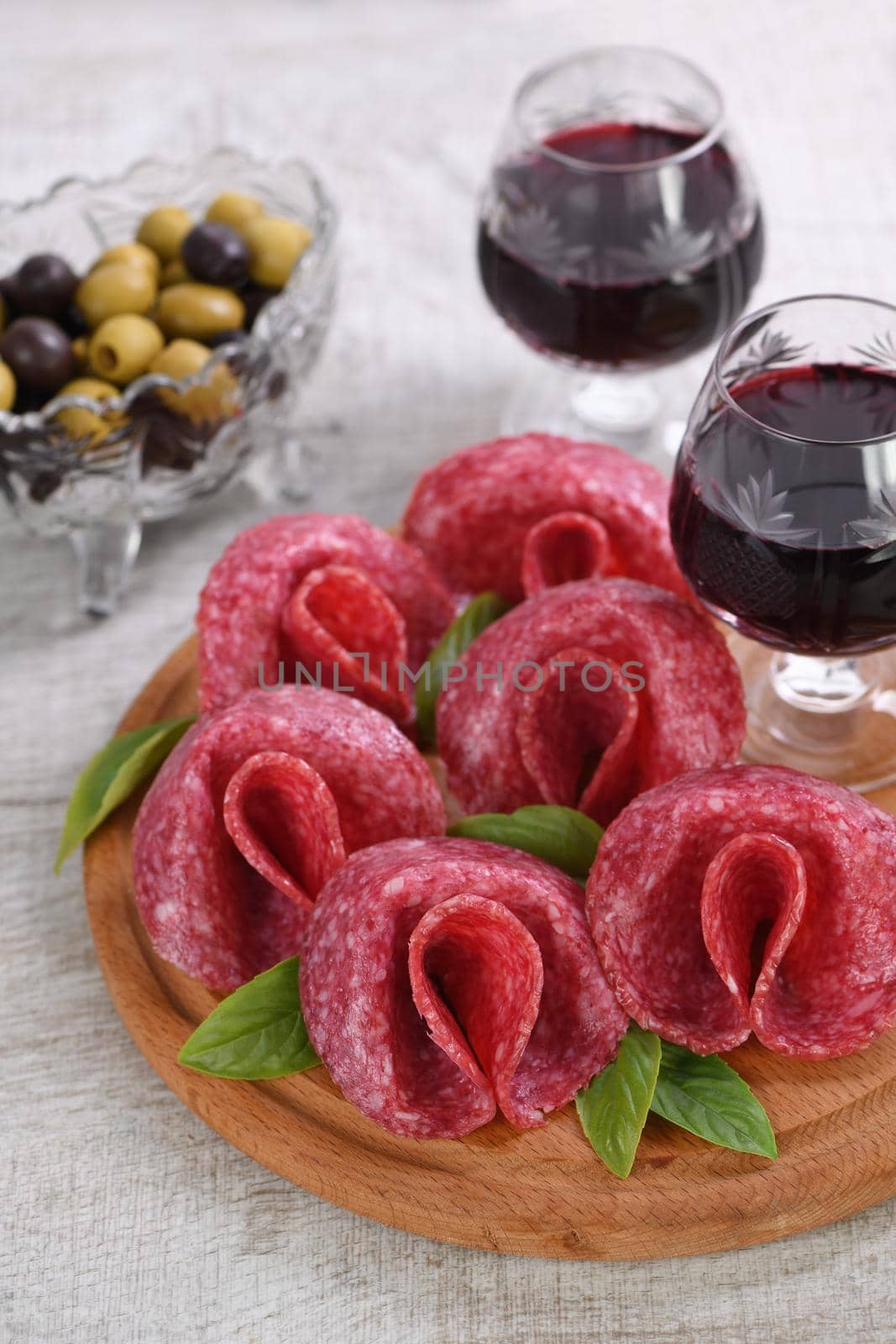 light meal snack from salami folded in the form of a flower with a glass sherry on a wooden dish. Close-up.