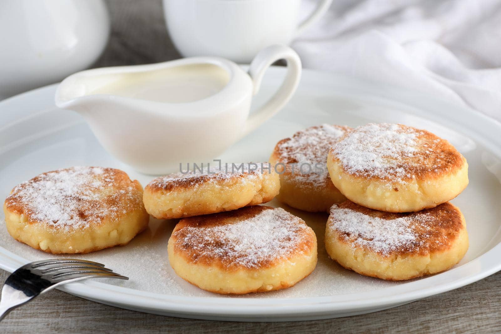 Breakfast. Cheese pancakes with sour cream sprinkled with powdered sugar on a white plate.