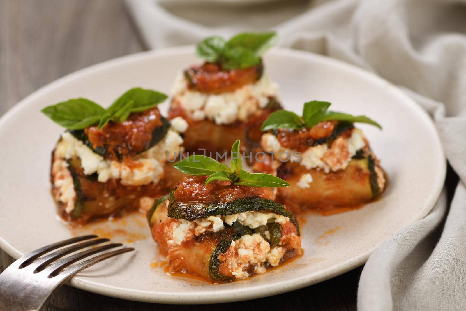Baked zucchini rolls stuffed with ricotta and basil under tomato-onion-carrot gravy 