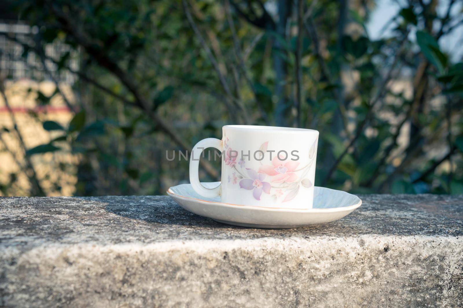 Coffee cup in morning sunlight. Summer fresh cool look. White coffee cup on saucer for hot drink on roof beam of a residential building with bokeh background.