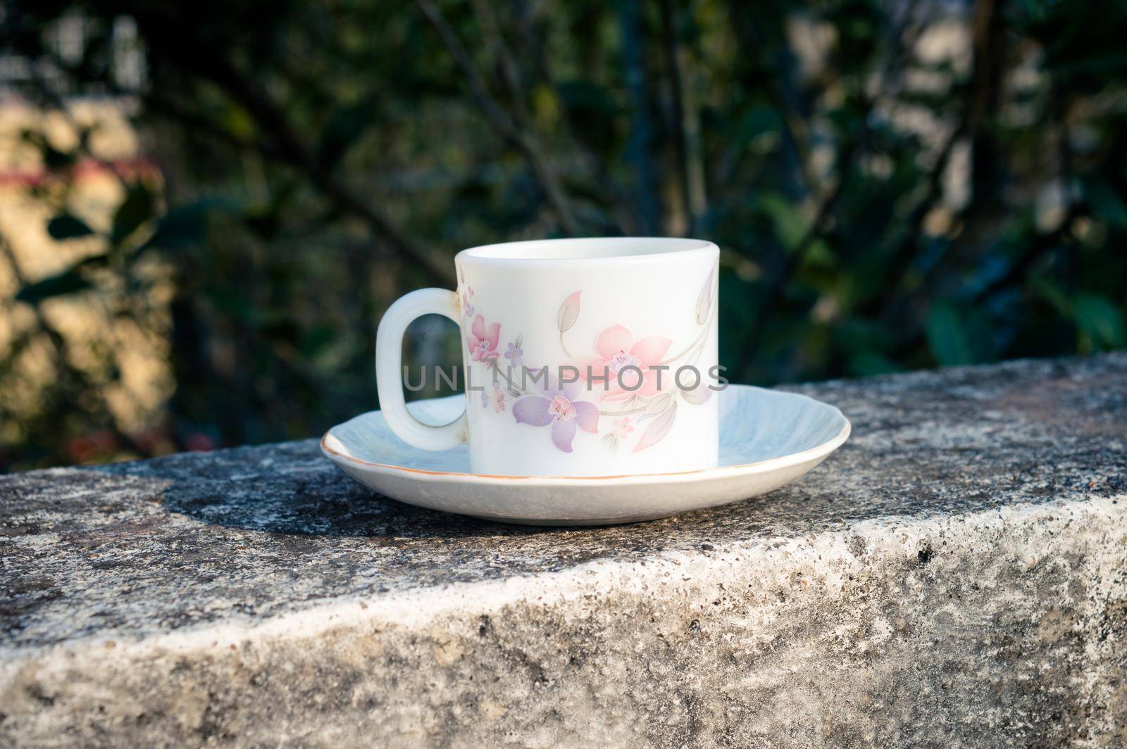 Coffee cup in morning sunlight. Summer fresh cool look. White coffee cup on saucer for hot drink on roof beam of a residential building with bokeh background. by sudiptabhowmick