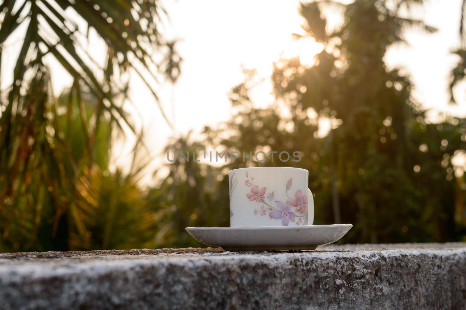 Coffee cup in sunset sunlight. Summer fresh cool look. White coffee cup on saucer for hot drink on roof beam of a residential building with bokeh city in the background.