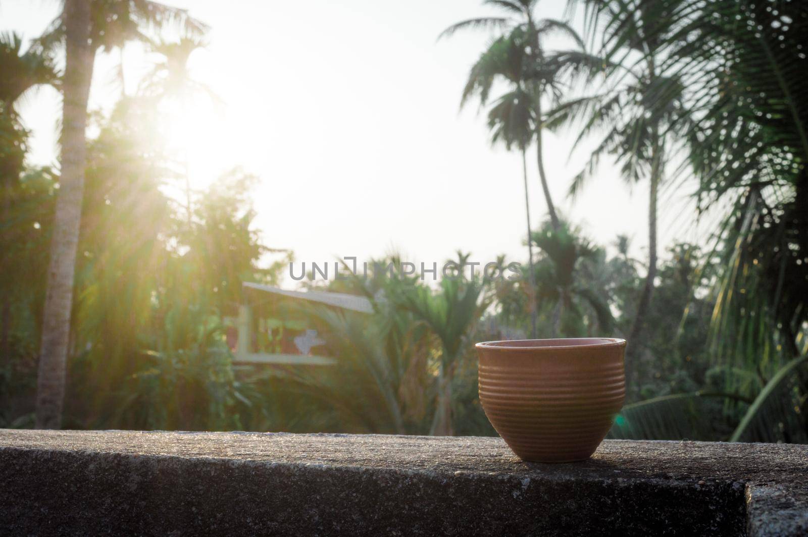 Coffee cup (Bhar) in sunset sunlight. Summer fresh cool look. Muddy mud tea cup made of clay for hot drink on roof beam of a residential building with bokeh city in the background. by sudiptabhowmick