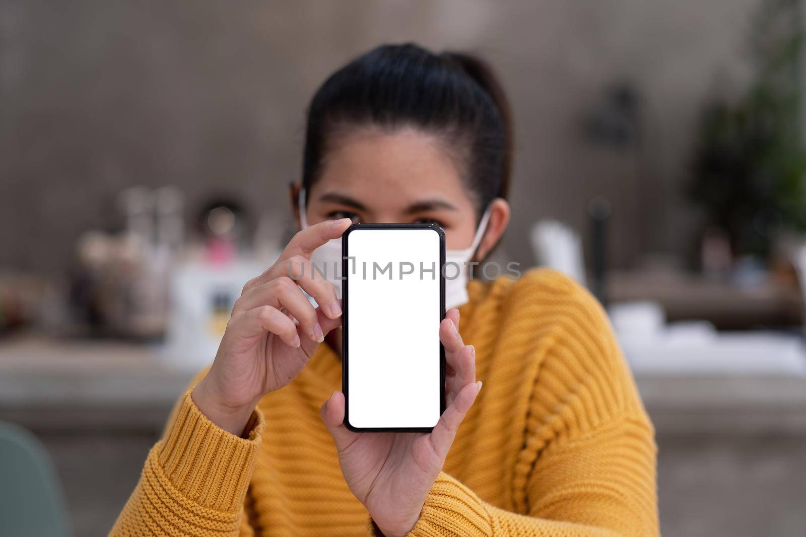 Mockup image of a beautiful woman wear mask while holding mobile phone with blank white screen