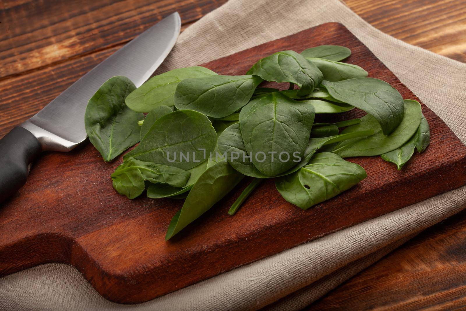 Heap of fresh green spinach and kitchen knife on the wooden board
