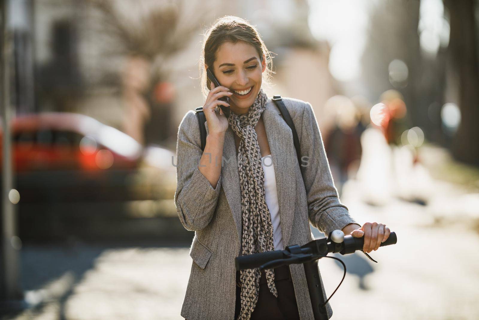 A young businesswoman using a smartphone while traveling with an electric scooter through the city.