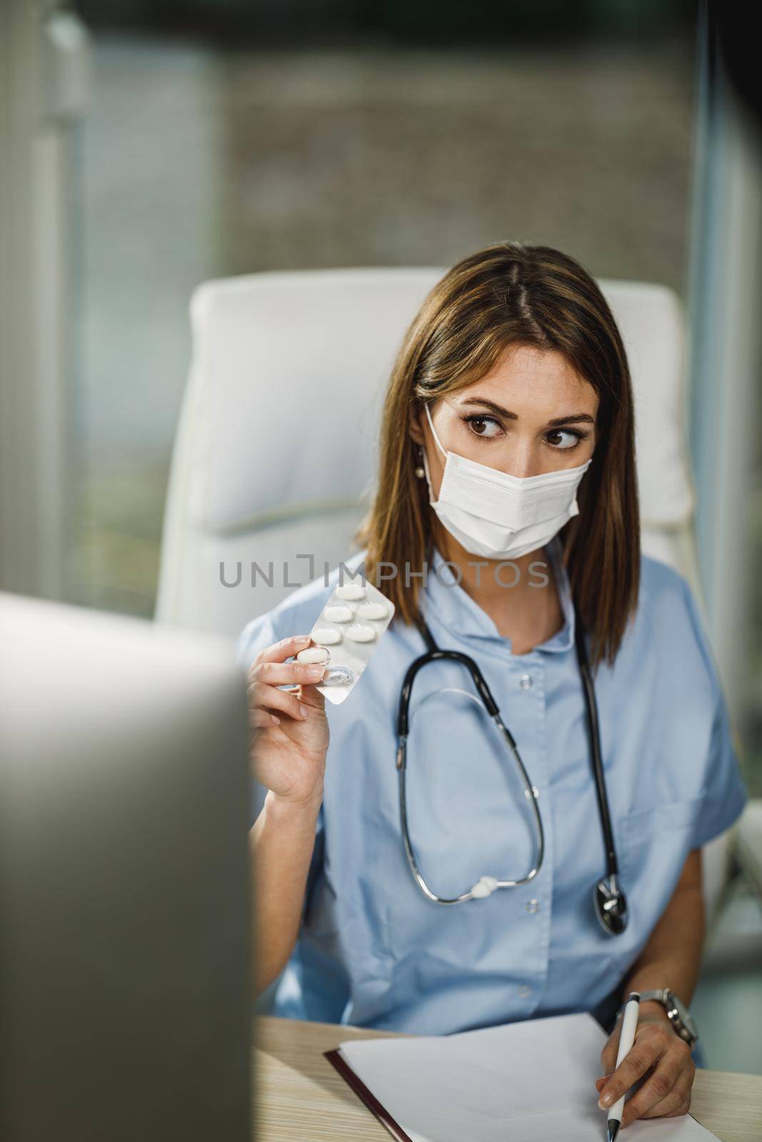 A female nurse with protective face mask having video call with patient on computer during COVID-19 pandemic.