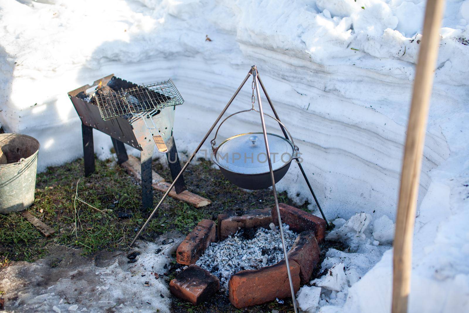 Over the fire hangs a pot in which to cook food. On a hook on a tripod, steam comes out of the pan. Winter Camping outdoor cooking