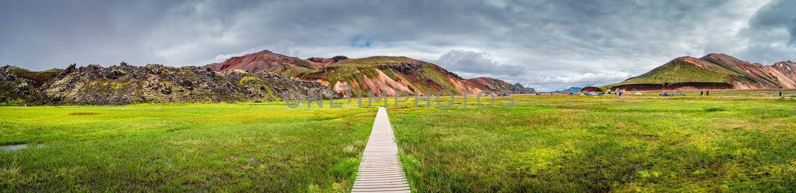 Panoramic view of colorful volcanic Landmannalaugar mountains, camping site and trail path at dramatic sky in Iceland