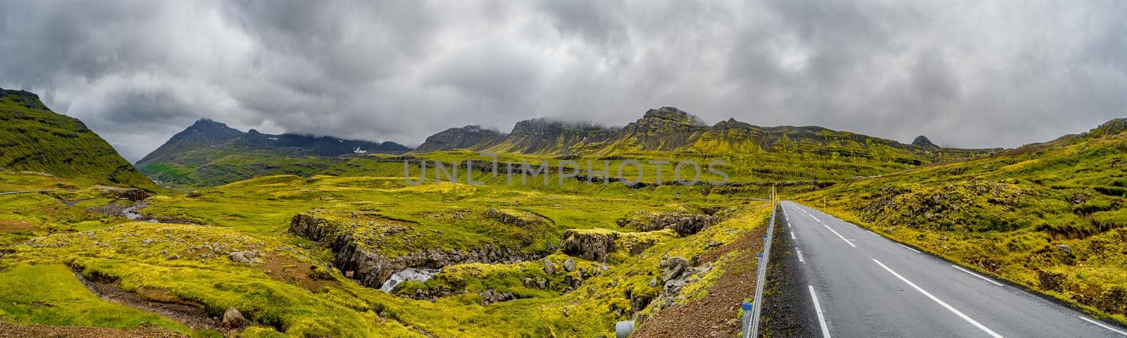 Panoramic view over lonely road through rough and greenish Icelandic landscape, Iceland, dramatic view of sky with clouds and rain