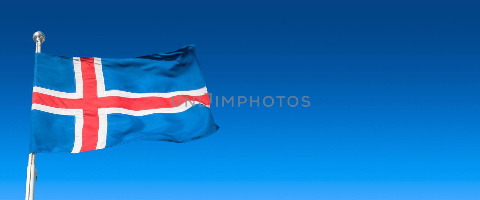 Banner with blue Icelandic national civil flag with red and white cross at blue sky background with copy space for text, closeup, details by neurobite