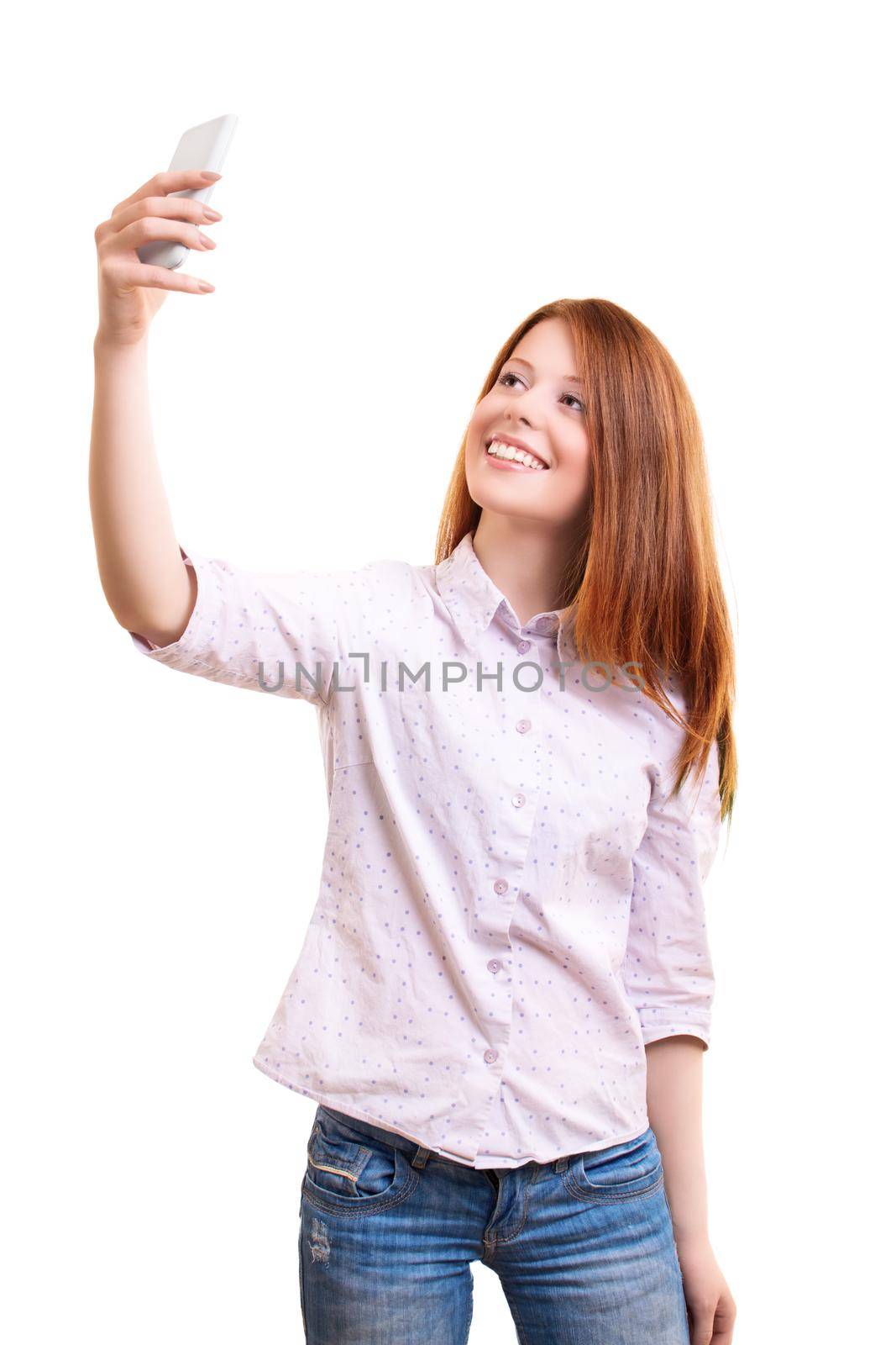 Portrait of a beautiful smiling young woman in smart casual clothes taking a selfie with her mobile phone, isolated on white background. Social media, communication concept.
