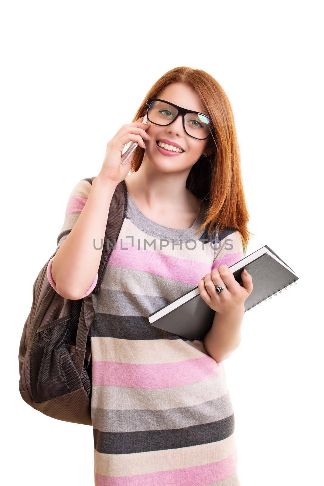 Smiling young fashionable female student with backpack holding a notebook and talking on a mobile phone, isolated on white background. Education and back to school concept. Technology and communication concept.
