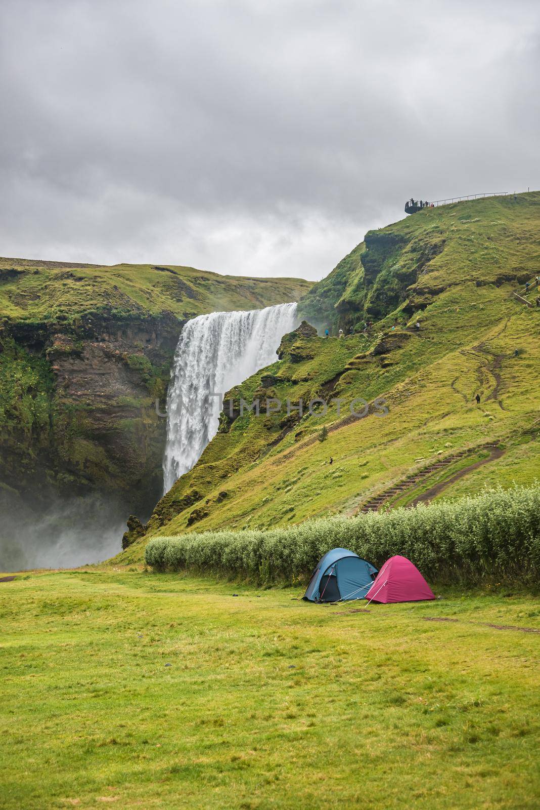 Wonderful, high and huge Skogarfoss waterfall and camping site with tents on South Iceland, summer by neurobite