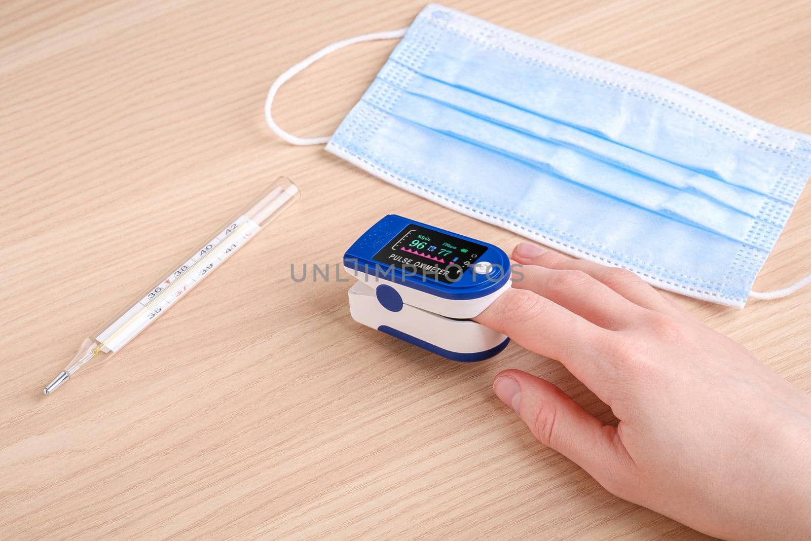 Person using pulse oximeter device near to thermometer and medical mask, healthcare monitoring concept