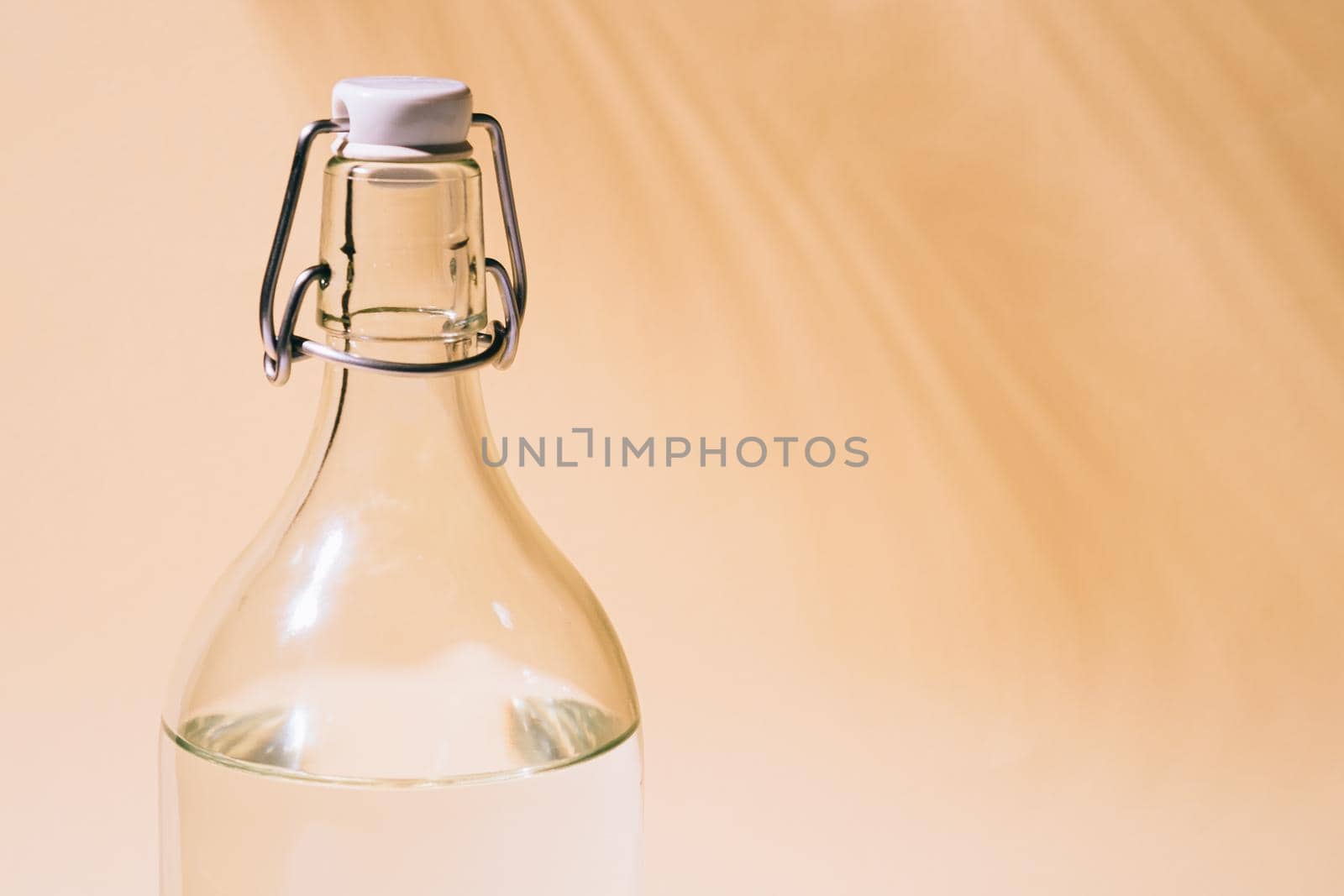 Glass bottle with water on pastel background with tropical palm leaf shadow