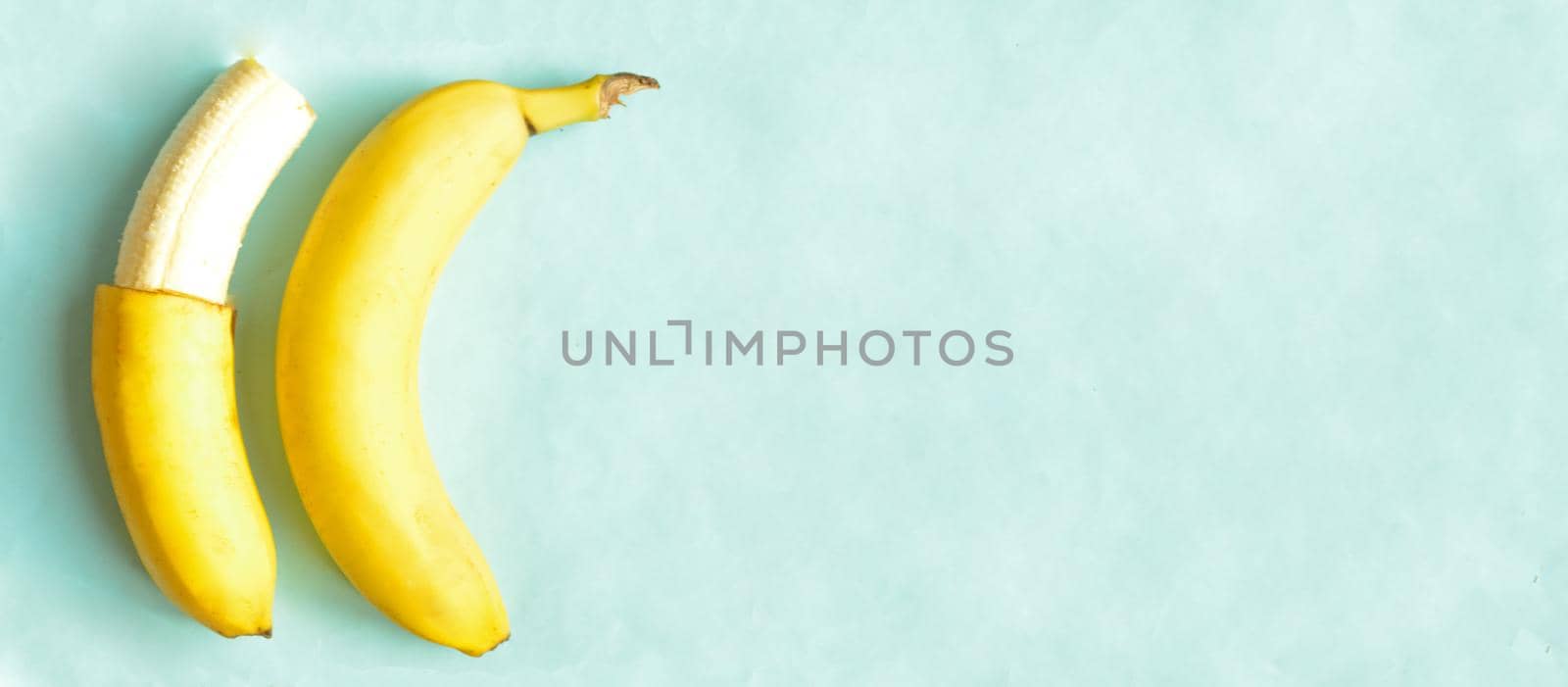 One partially peeled banana and one whole on blue background, copyspace.Sweet tropic fruit for hot summer