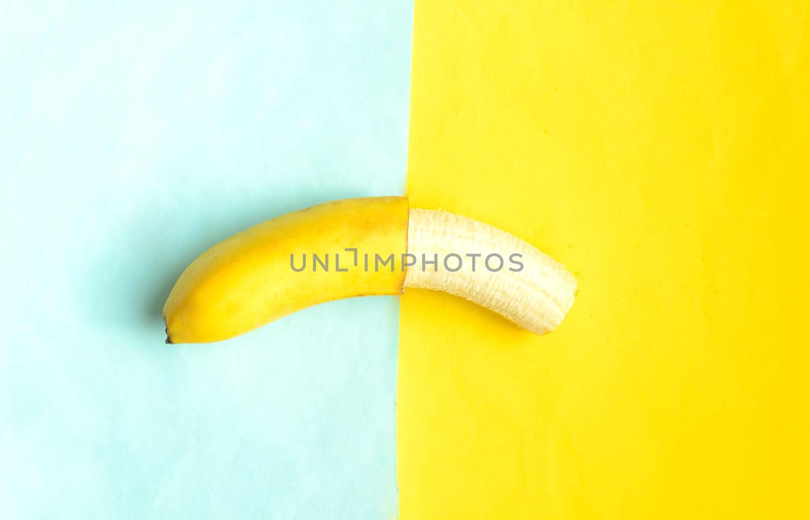 Partially peeled banana on blue yellow background.Tropic summer fruit
