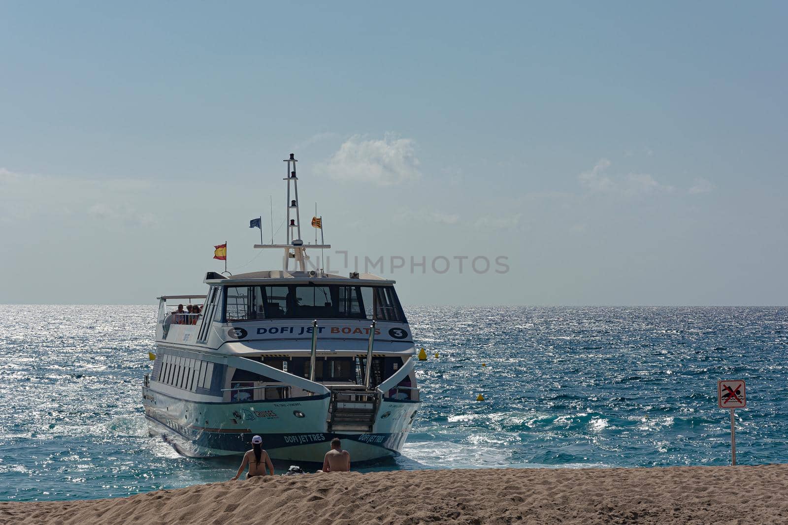 Lloret De Mar, Spain - April 03, 2021: A pleasure boat docks at a sandy beach by Grommik